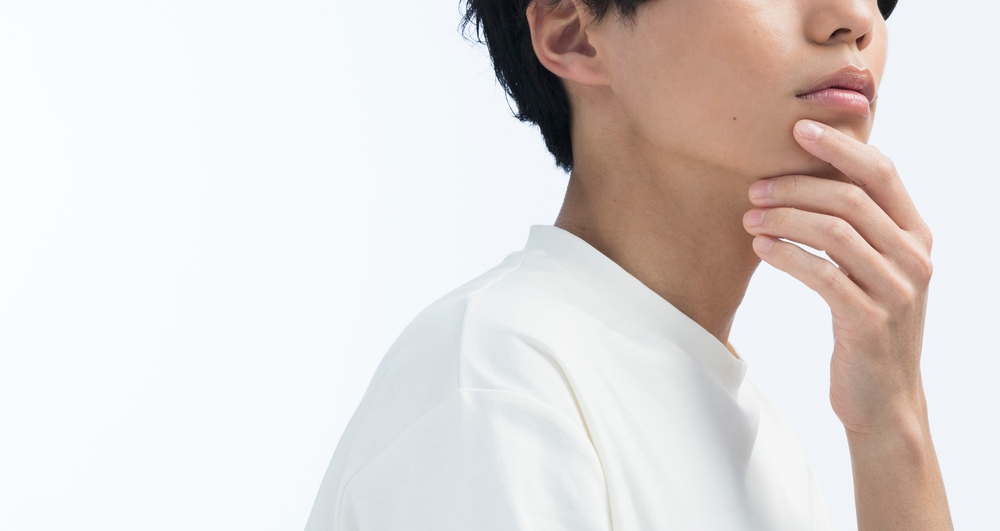 Cropped view of a young man in a white t-shirt resting his hand on his chin against a clean white background